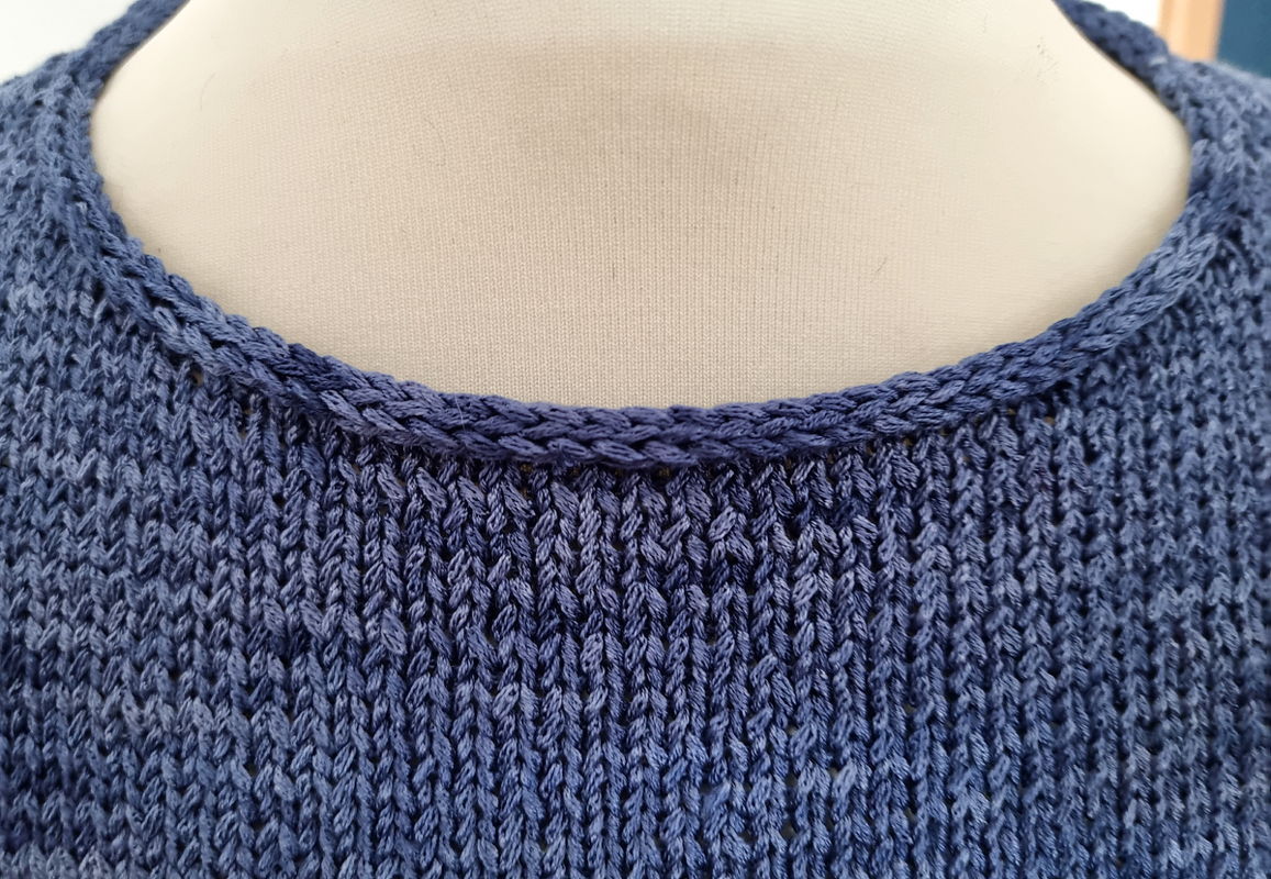 Nahaufnahme eines blauen gestrickten Damenshirts, Fokus auf gerippten Rundhalsausschnitt und Maschenbild.