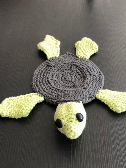 Gehäkelte Schildkröte mit dunkelgrauem Panzer und hellgrünen Flossen auf dunklem Untergrund
