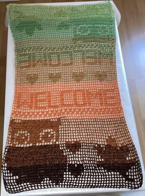 Handgehäkelter Filet-Tischläufer mit 'WELCOME'-Schriftzug, Herz-Motiven, Tierfiguren und Farbverlauf in Grün, Orange und Braun
