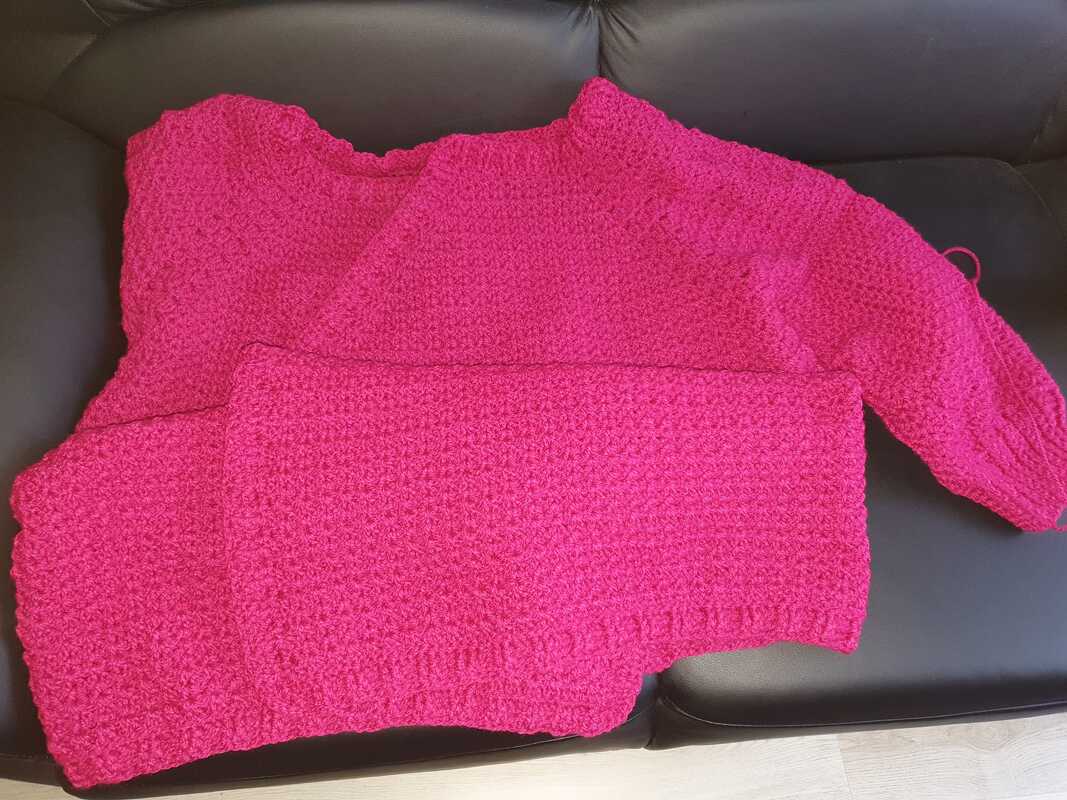 Gehäkelter Damenpullover in Fuchsia mit strukturiertem Muster, flach liegend.