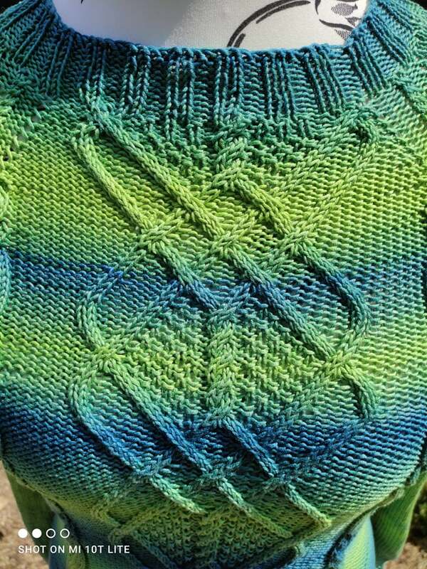 Nahaufnahme eines gestrickten Damenpullovers mit Rauten-Zopfmuster und Blau-Grün-Farbverlauf, mit sichtbarem Rippenbündchen am Hals