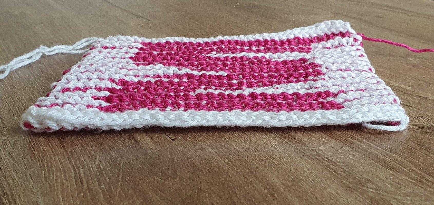 Gestrickte rechteckige Probe in Weiß und Pink auf Holz