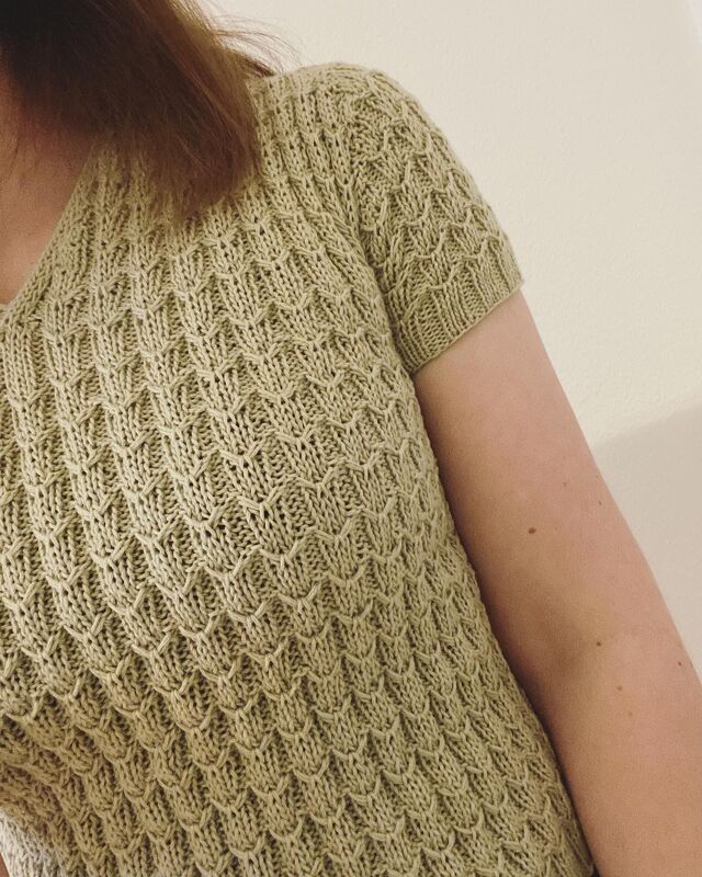 Close-up of a sage green short-sleeved knitted top with textured stitch pattern and V-neckline.