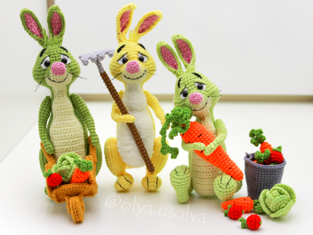 Three crocheted amigurumi rabbits, two green and one yellow, with miniature garden tools and crocheted vegetables