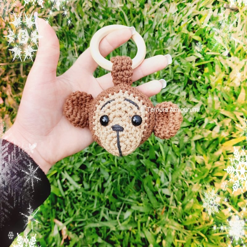 Close-up of a mini crocheted monkey head keychain with a wooden ring, held between fingers, showing the crocheted attachment