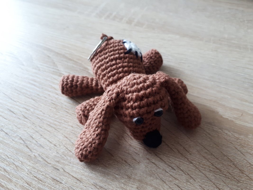 Brauner gehäkelter Hunde-Schlüsselanhänger mit Schlappohren auf Holzfläche