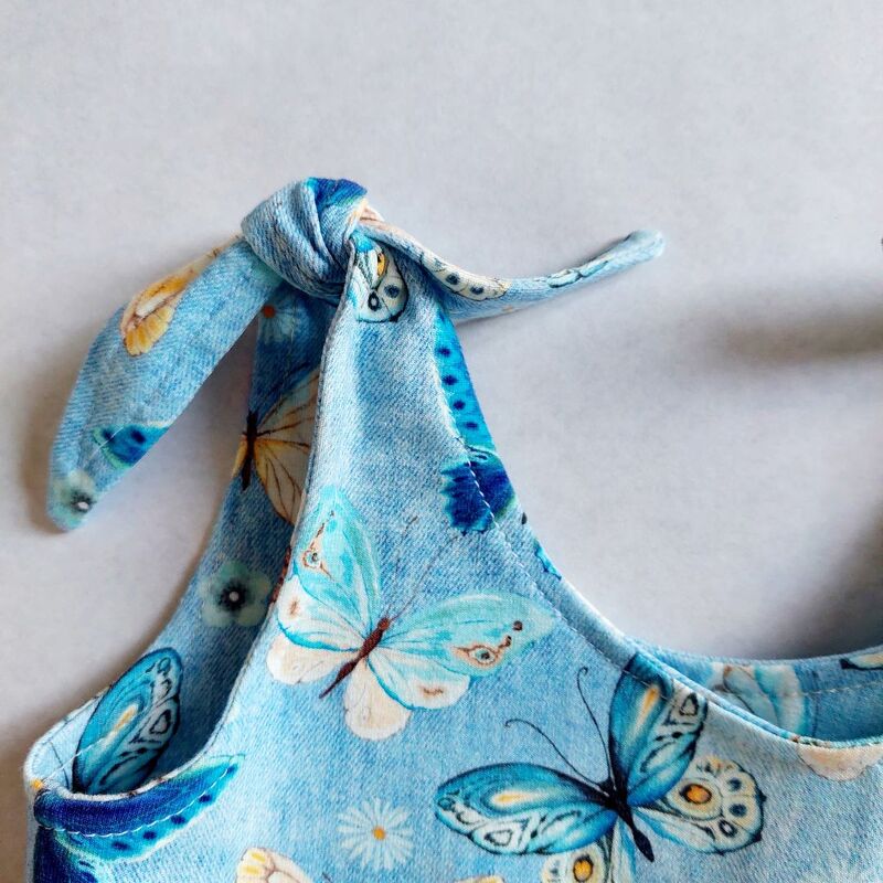 Nahaufnahme hellblaues Kinder-Trägerkleid mit Schmetterlingsmuster und geknotetem, verstellbarem Träger