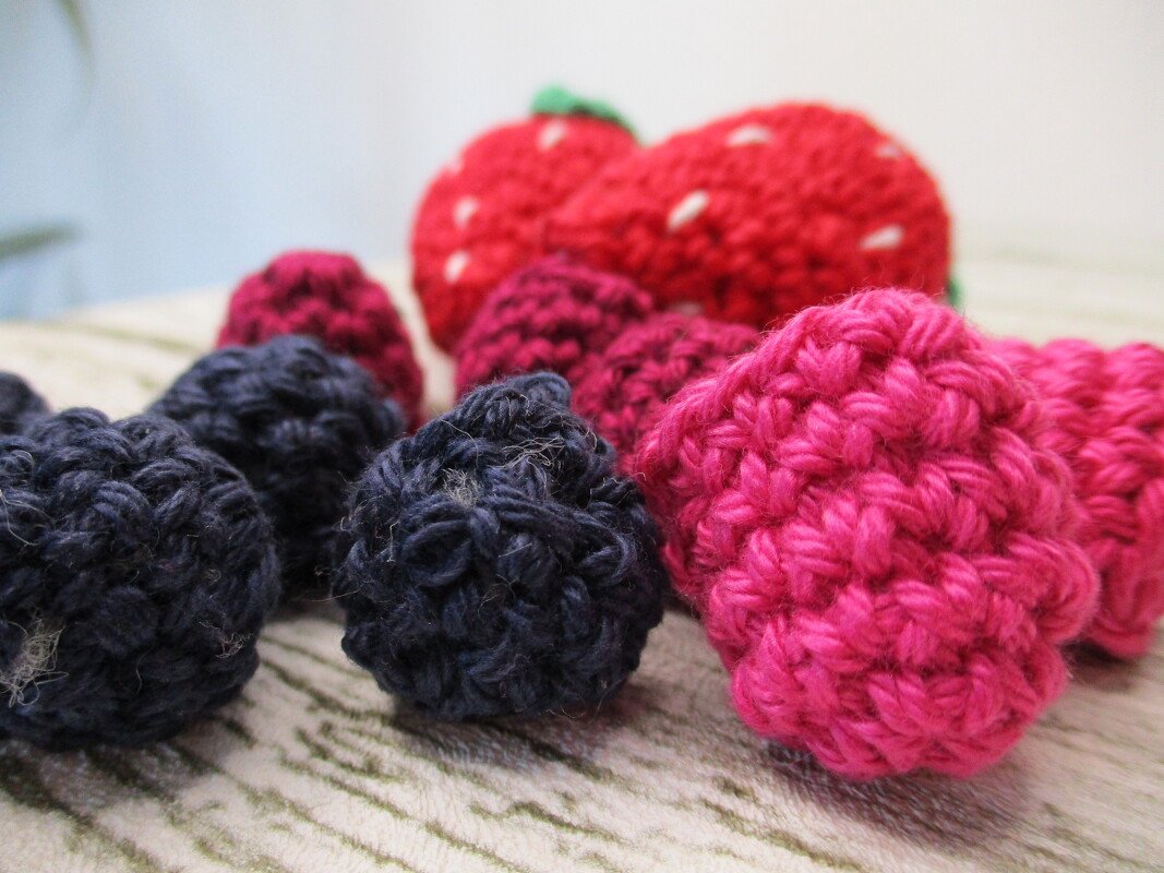 Nahaufnahme gehäkelter roter Erdbeeren und dunkler Beeren