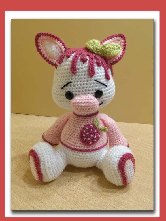 Weiß-rosa Amigurumi-Schweinchen mit Erdbeer-Applikation und grünen Blättern auf dem Kopf, gehäkelt