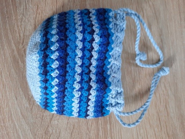 kleine gehäkelte beuteltasche mit blauen und weißen streifen und kordelzug auf holzuntergrund