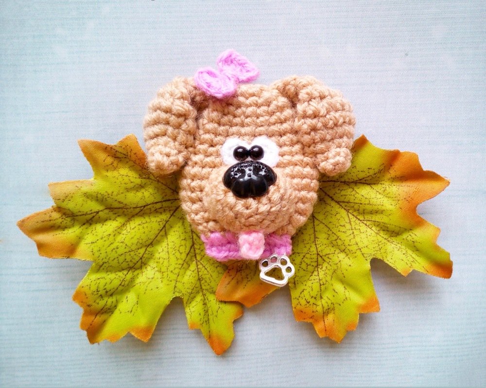 Compact beige crochet dog face with pink bow, button nose, bead eyes, and paw charm