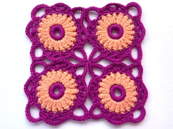 Viereckiges Häkelmotiv aus vier runden Blüten in Pfirsich und Magenta auf weißem Hintergrund