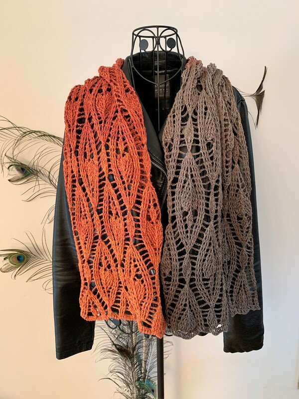 Two long openwork crochet scarves with leaf-stitch repeats, one rust and one taupe, displayed on a dress form.