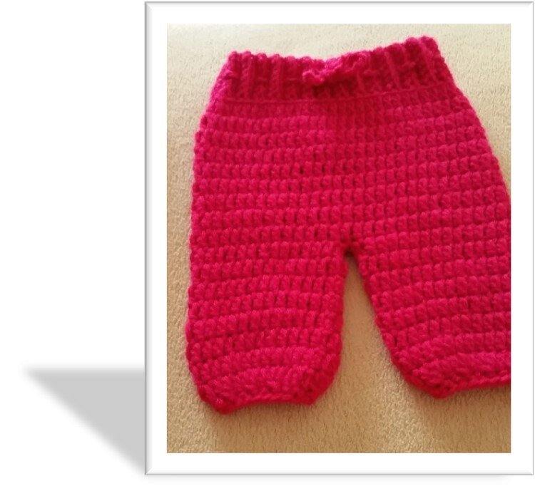 Gehäkelte pinke Babyhose, flach liegend, mit sichtbarer Struktur und elastischem Bündchen