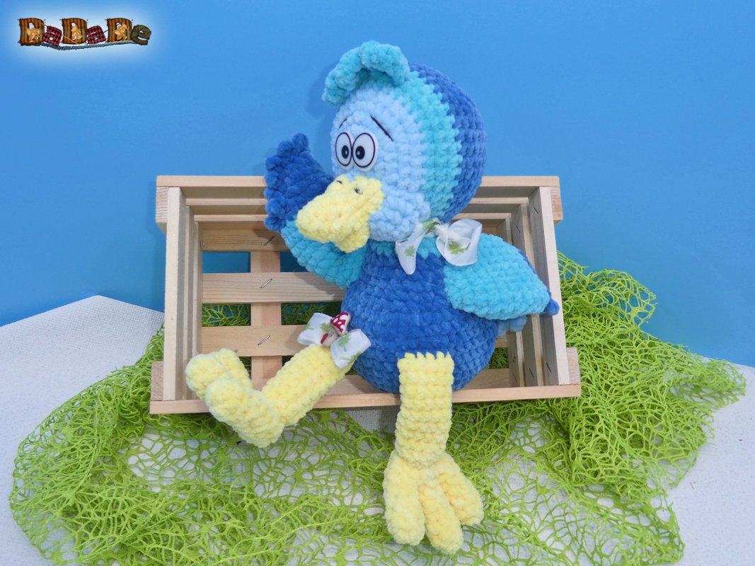 Gehäkelte blaue und gelbe Amigurumi-Ente sitzt in einer Holzkiste