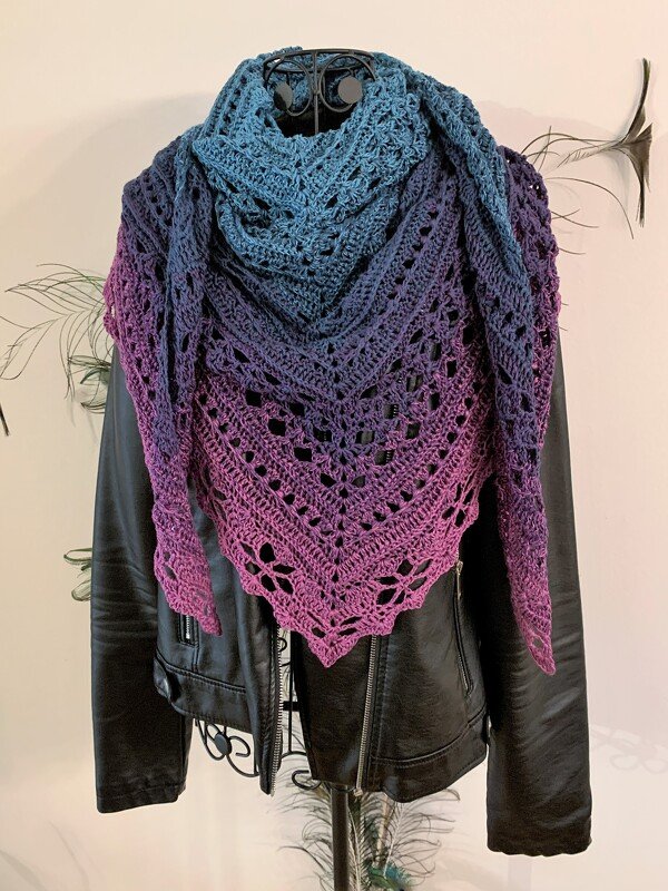 Blue-to-purple ombre crochet triangle shawl with lace pattern, draped over a black leather jacket on a mannequin.