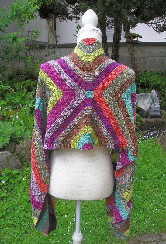 Bunt gestreiftes gestricktes Dreieckstuch auf Schneiderpuppe vor Gartenkulisse