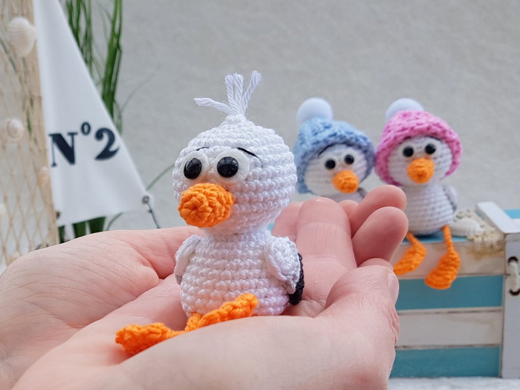 Nahaufnahme eines weißen gehäkelten Amigurumi-Vogels mit orangefarbenem Schnabel und Füßen in beiden Händen.