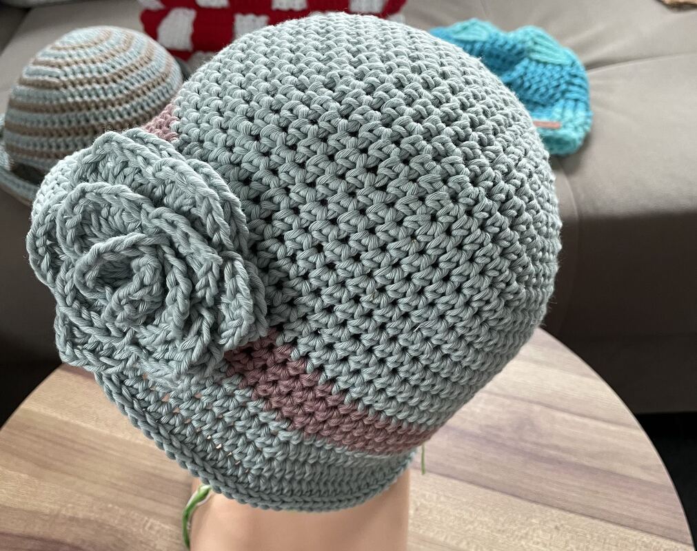 Gehäkelte mintgrüne Damenmütze mit seitlicher Blüte und rosa Streifen auf Kopfmodell