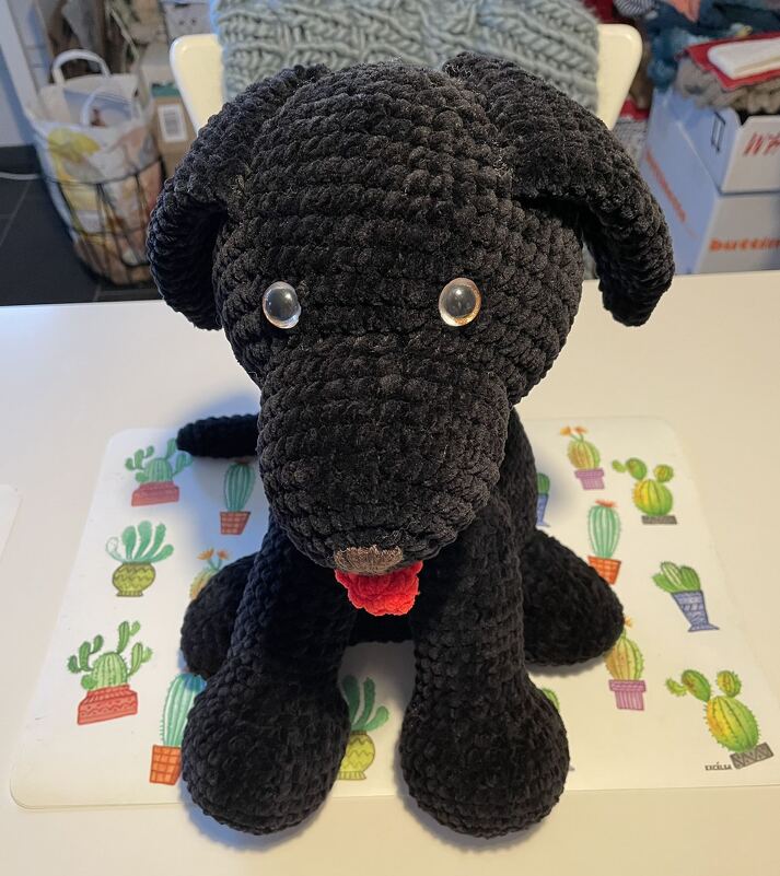 Plüschiger, gehäkelter schwarzer Hund mit roter Zunge und glänzenden Augen