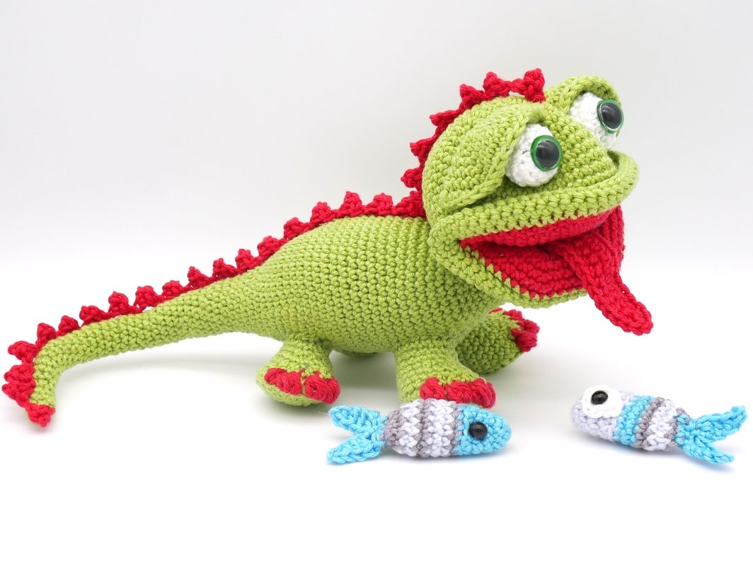 Gehäkelter grüner Drache mit roten Stacheln und zwei kleinen blauen Fischen