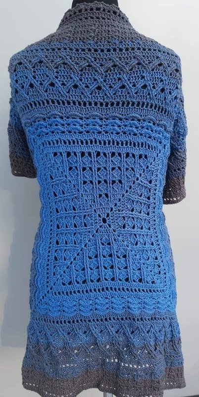 Rückenansicht eines gehäkelten Damenponchos in Blau-Grau mit quadratischem Ajourmotiv und Muschelkante