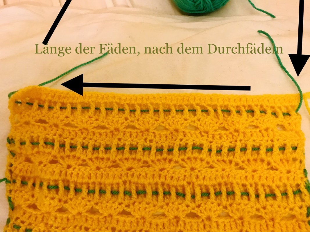 Detail einer gelben Häkelarbeit mit grünem Garn, das durch die Reihen gezogen wird als Arbeitsschritt.