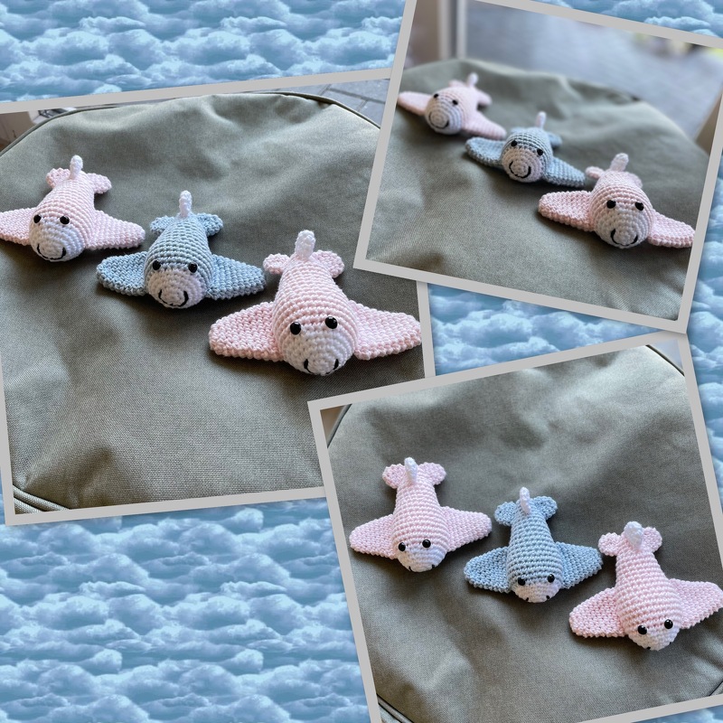 Drei gehäkelte Amigurumi-Manta-Rochen (zwei rosa, einer hellblau) auf olivgrünem Stoff