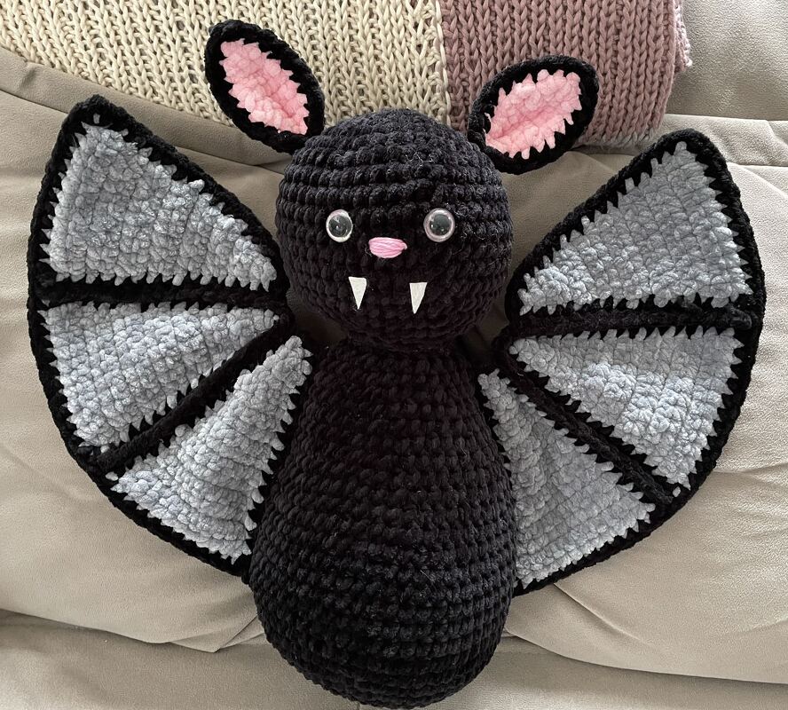 Schwarze gehäkelte Fledermaus mit grauen Flügeln, rosa Ohren und weißen Zähnchen