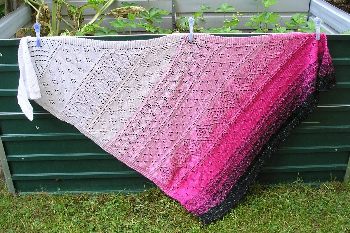 Gestricktes Dreieckstuch mit Verlauf von Weiß zu Pink bis Schwarz und sichtbaren Lochmustern, im Freien aufgehängt