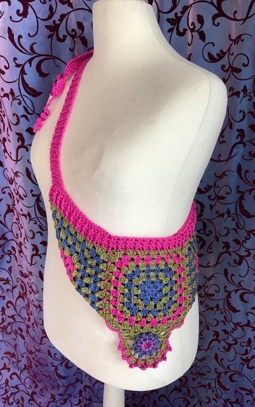 Gehäkelte Umhängetasche aus Granny‑Squares in Pink, Blau und Olivgrün auf einer Schneiderpuppe.