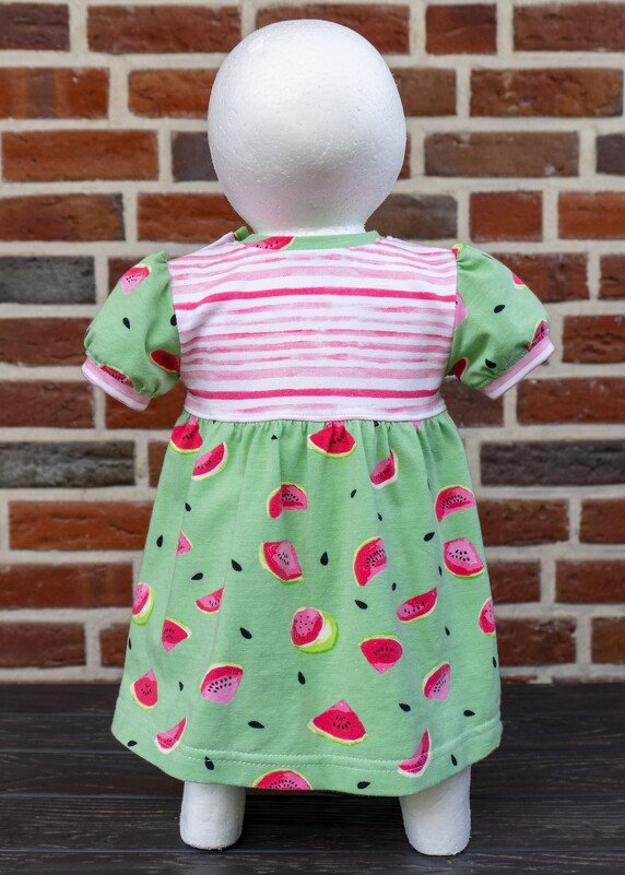 Rückansicht eines Babykleids mit grünen Wassermelonen und rosa-weiß gestreiftem Oberteil auf einer Schaufenpuppe.