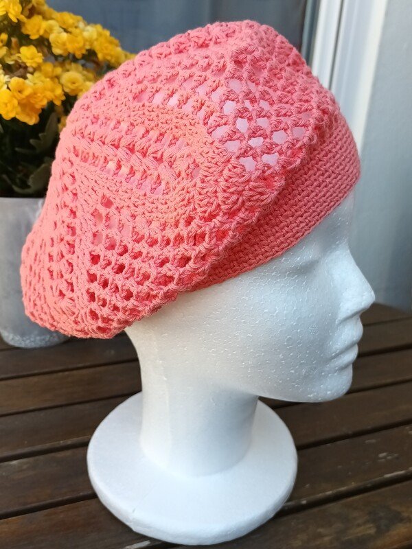 Nahaufnahme einer gehäkelten korallenfarbenen Baskenmütze mit Lochmuster auf einem Styroporkopf