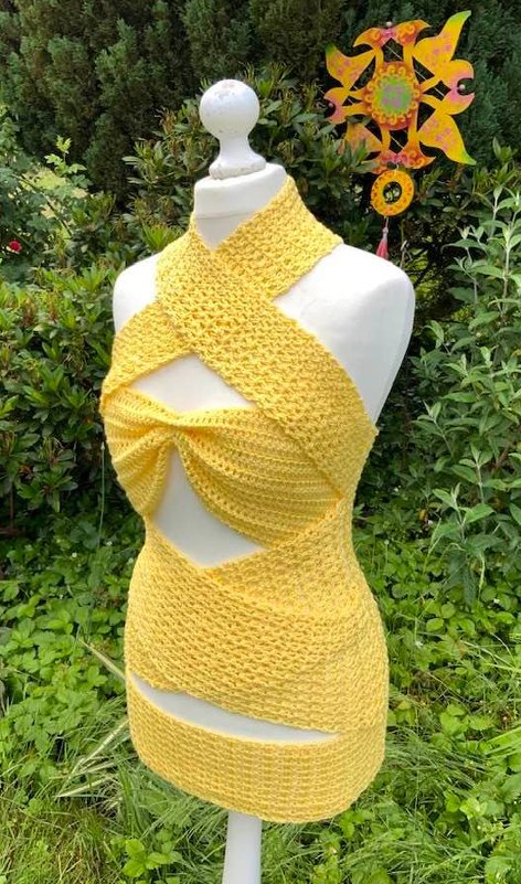 Gelbes gehäkeltes Kleid oder Tunika mit Neckholder-Ausschnitt, gekreuzten Trägern und Cut-Outs an Seiten und Saum auf einer Schneiderpuppe vor grünem Garten