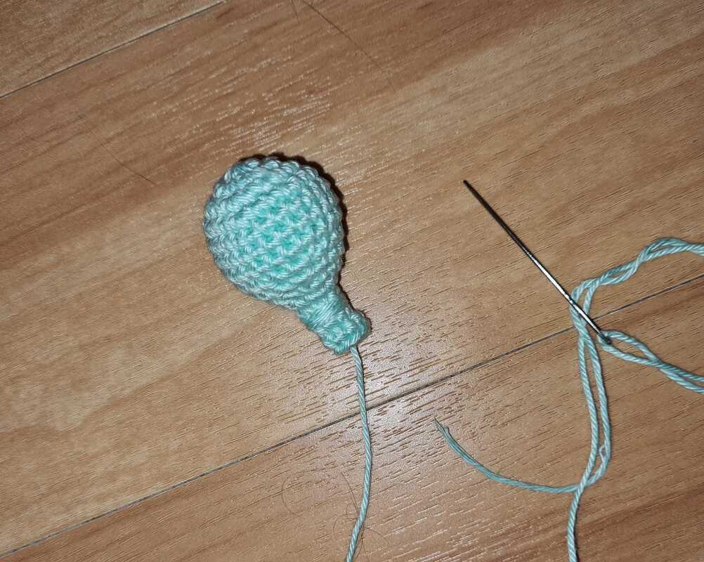 Hellblaues gehäkeltes Amigurumi-Teil mit Stopfnadel auf Holzoberfläche
