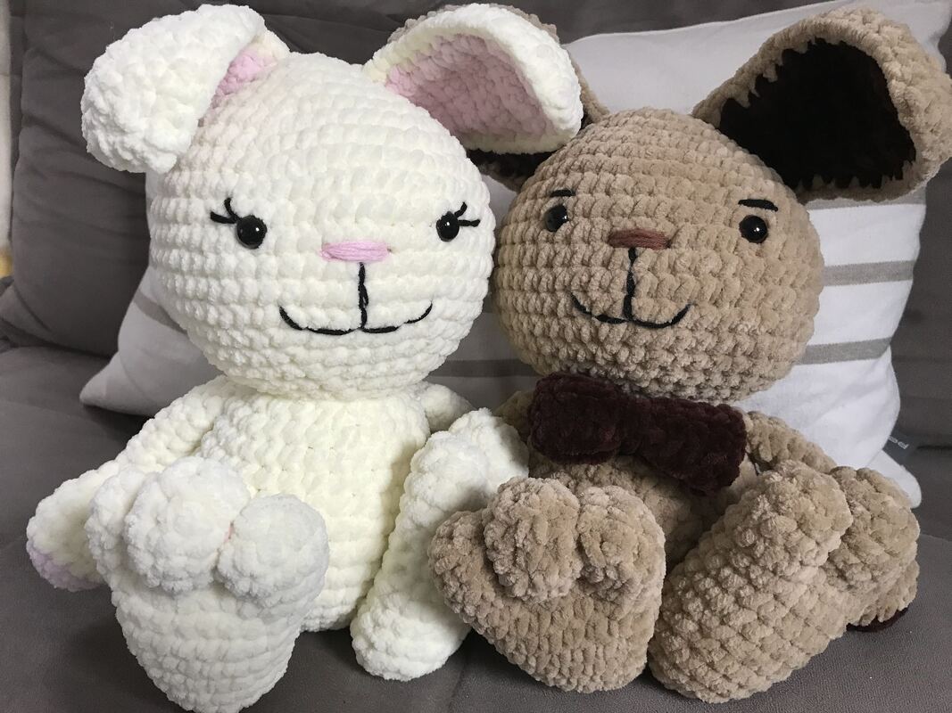 Zwei gehäkelte Amigurumi-Hasen, einer weiß und einer beige, sitzen nebeneinander