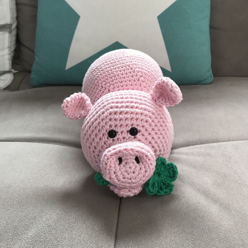 Rosa gehäkeltes Schweinchen Amigurumi mit grünem Kleeblatt auf grauem Sofa