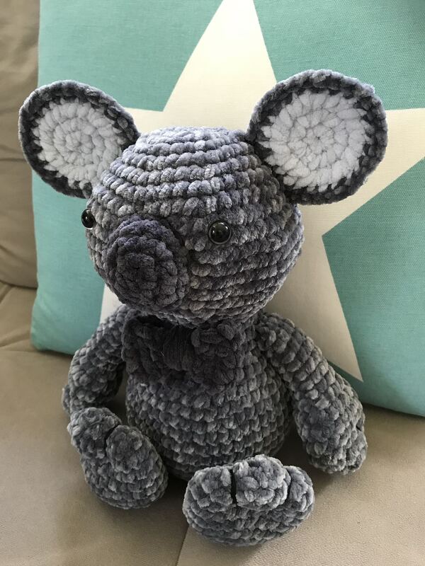 Gehäkelter grauer Amigurumi-Koala aus Samtgarn, sitzend vor einem türkisfarbenen Kissen