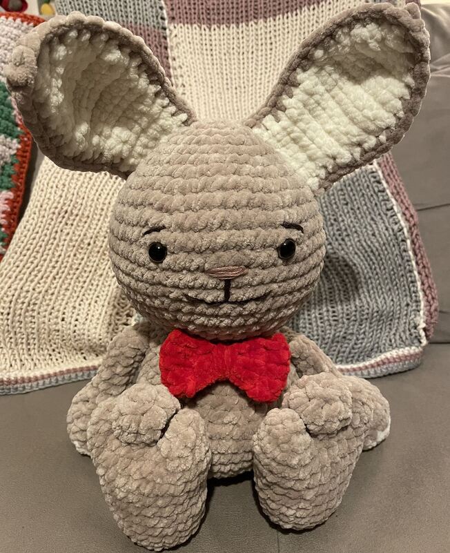 Nahaufnahme eines gehäkelten Amigurumi-Hasen mit großen Ohren und roter Fliege, Details von Kopf und Körper sichtbar