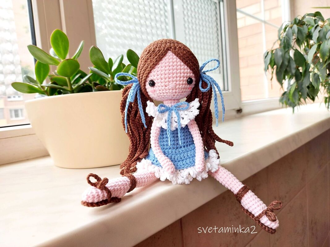crocheted amigurumi doll with brown yarn hair and blue dress sitting on a windowsill