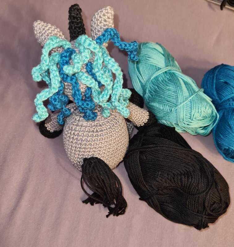 Gehäkelte spiralförmige Mähne aus türkis-blauen Garnsträngen am Einhornkopf mit schwarzen Garnknäueln
