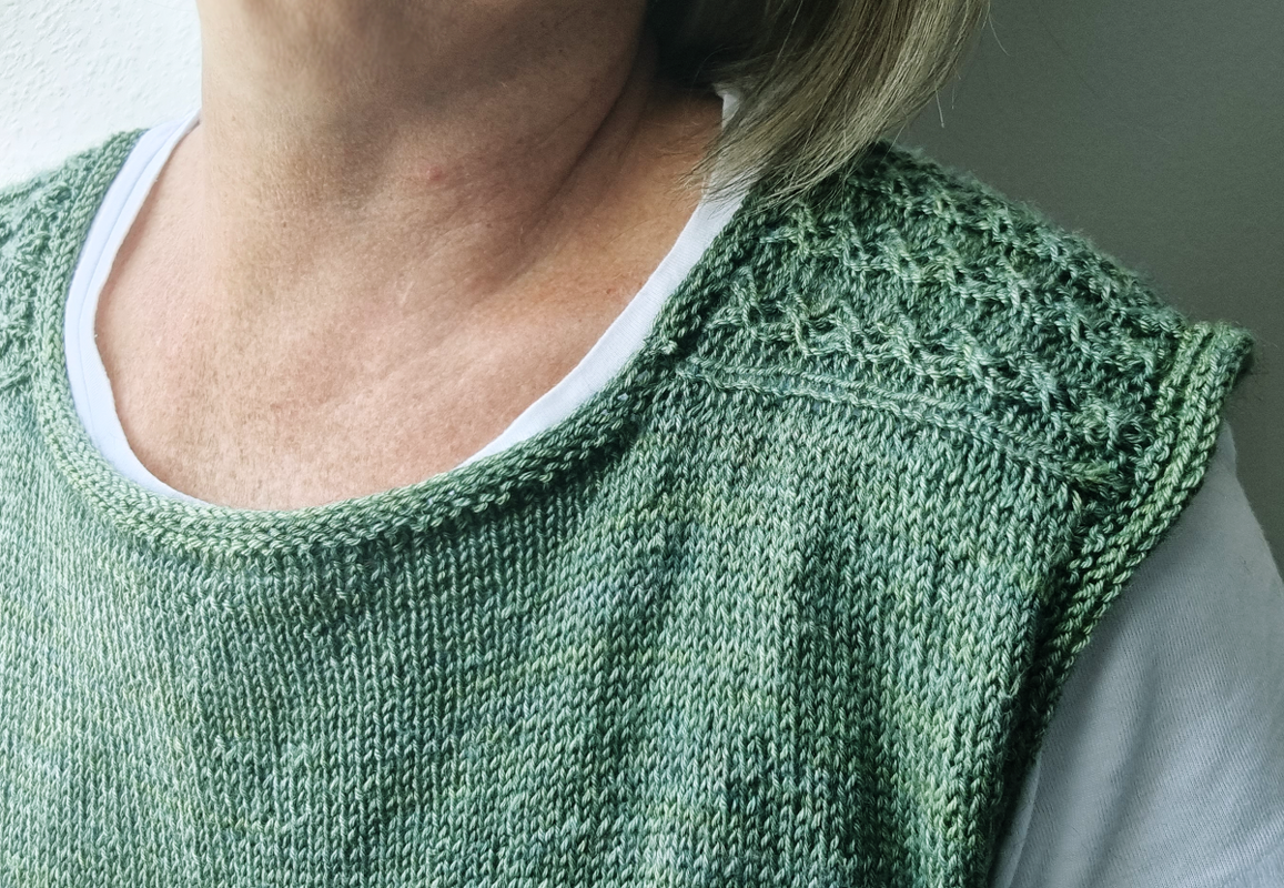 Grünes, ärmelloses Stricktop mit Strukturmuster an der Schulter; darunter ein weißes T‑Shirt.