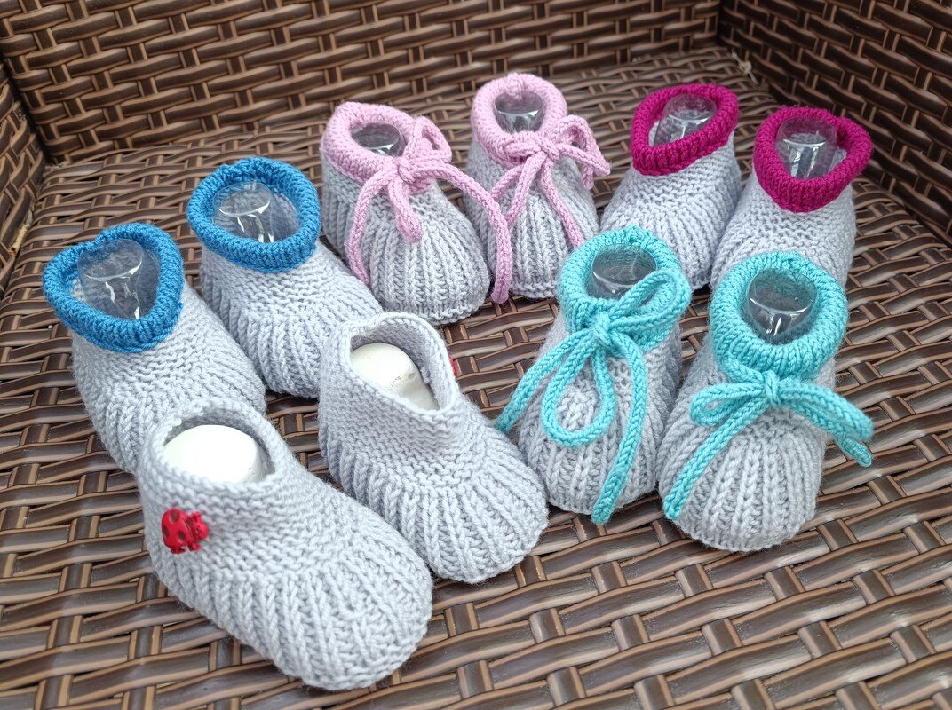 Mehrere hellgraue, gestrickte Babyschuhe mit bunten Bündchen in einem Korb.