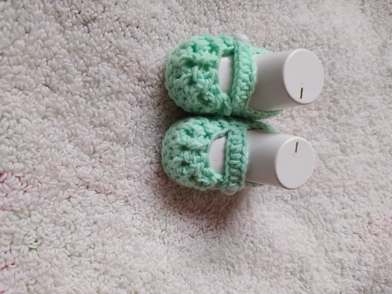Pair of mint-green crochet baby booties with straps on white forms