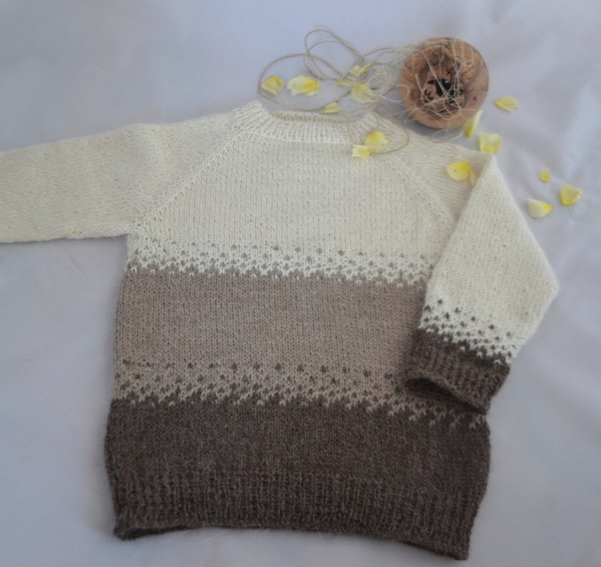 Gestrickter Kinderpullover in Creme, Beige und Braun mit Raglanärmeln, liegend