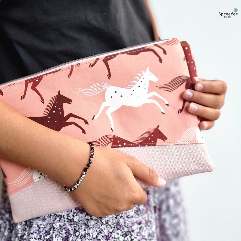 Flache Reißverschluss-Pouch in Rosé mit weißen und braunen Pferde-Silhouetten und hellrosa Bodenstreifen, in Händen gehalten
