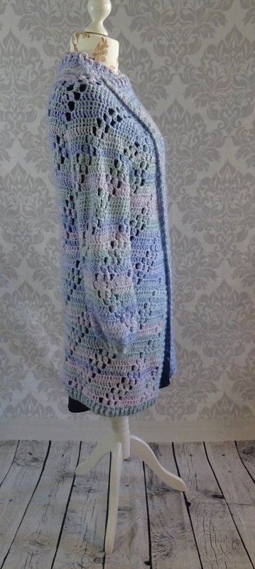 Langer gehäkelter Cardigan in Pastellfarben mit offenem Lochmuster auf einer Schneiderpuppe.