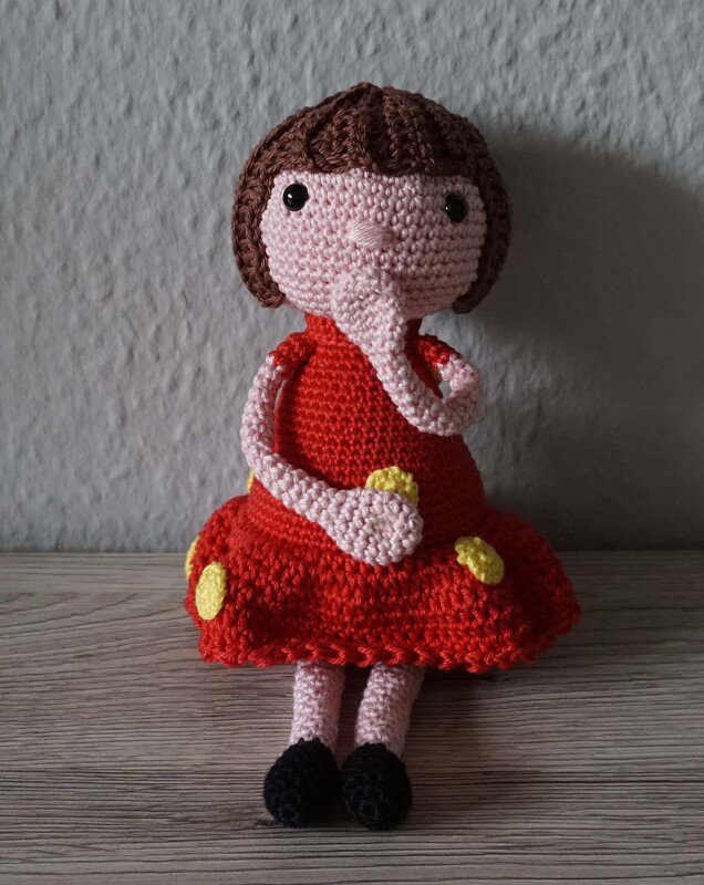 Gehäkelte Amigurumi-Puppe mit Rüssel, rotem Kleid, braunem Haar und schwarzen Schuhen