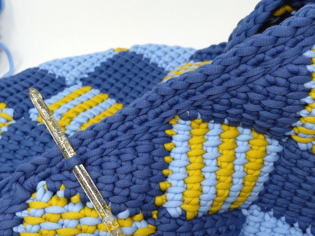 Detailaufnahme dichten Häkelstichs aus Jersey-Garn in Blau und Gelb mit transparenter Häkelnadel