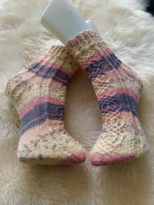 Kurz gestrickte Socken in Pastellfarben mit Streifen und feinem Strukturmuster, präsentiert auf hellem, flauschigem Untergrund.